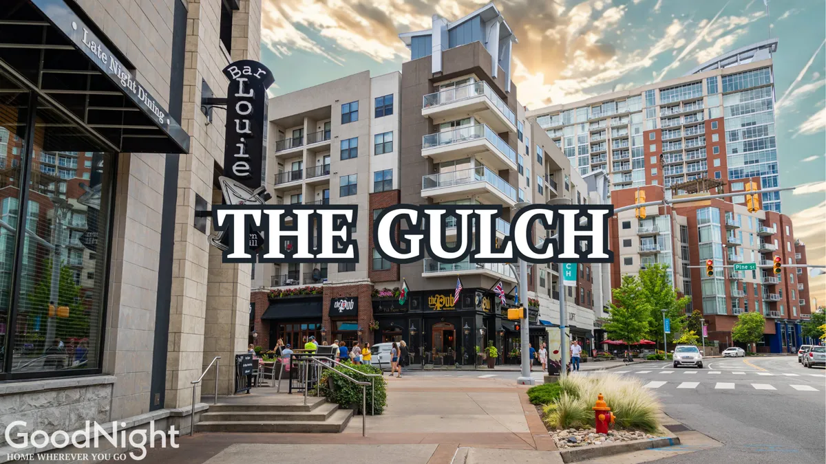 A lively city streetscape featuring modern apartment buildings, outdoor dining at Bar Louie, bustling sidewalks, and boutique storefronts. The scene conveys the energy of a vibrant neighborhood, with people socializing, shopping, and enjoying the nightlife.
