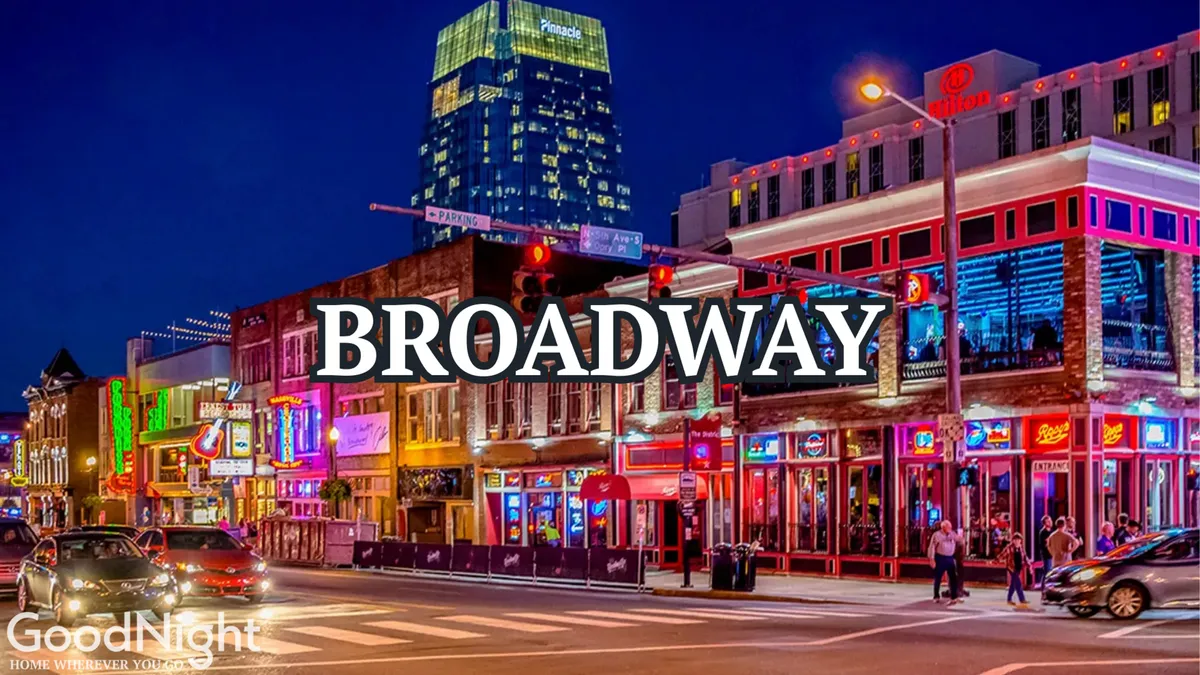 A bustling nighttime street scene with illuminated neon signs, people walking along the sidewalks, and cars passing by. The energy from the vibrant city nightlife is palpable, suggesting a lively area filled with music, dining, and entertainment.