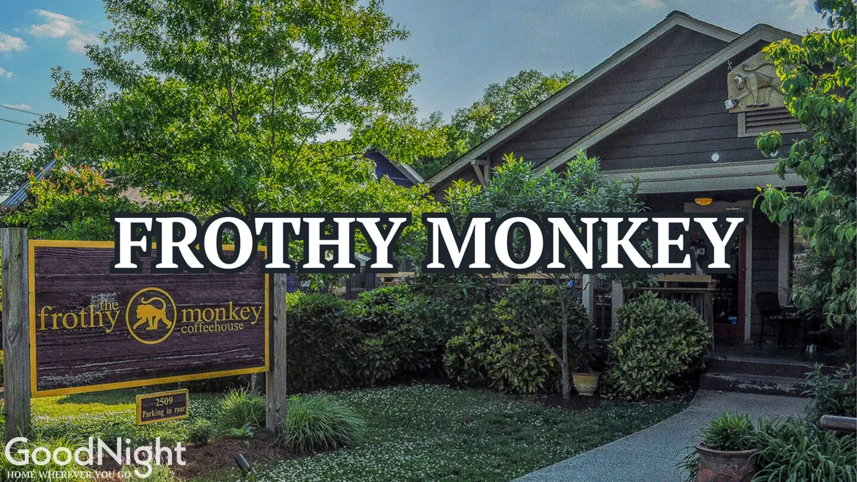 A warm, inviting exterior shot of Frothy Monkey, a popular coffee shop, featuring its distinctive signage, landscaped garden, and patio seating. The space suggests a vibrant street life and community gathering spot.