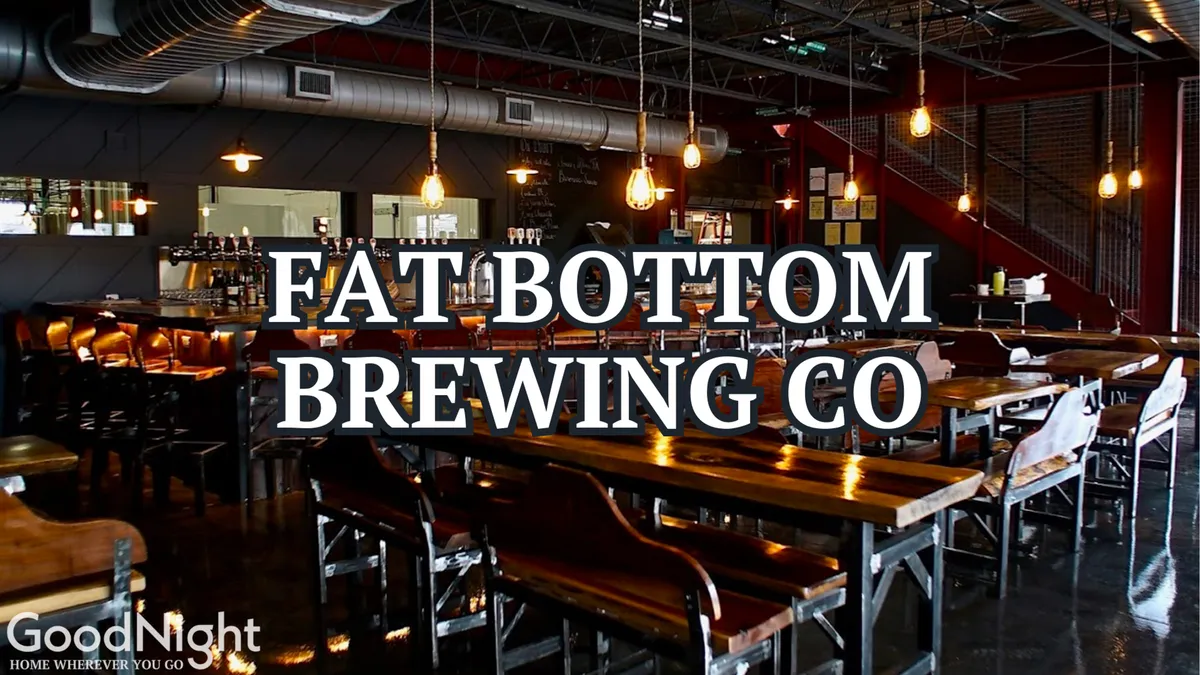 An inviting interior of a craft brewery or bar, featuring industrial accents, long wooden tables, a well-lit bar area, and groups socializing over drinks. The communal setup and casual ambiance suggest a popular gathering spot for sampling local beers and enjoying themed nights or live music.