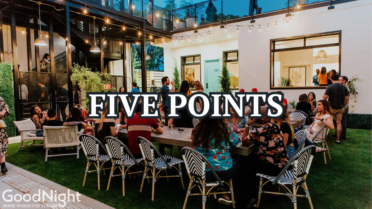A bustling outdoor patio scene with a large group of people celebrating under decorative string lights and surrounded by comfortable seating. The joyful expressions and communal atmosphere make it clear this is a prime spot for outdoor dining and late-night gatherings.
